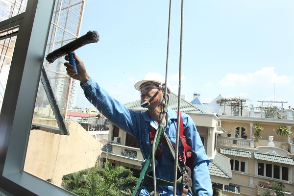 Nhân viên Pan Services Hà Nội thực hiện vệ sinh kính mặt ngoài tòa nhà cao tầng với dây cáp hỗ trợ